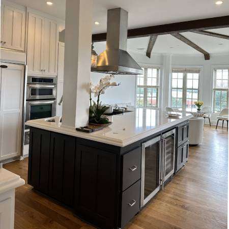 Kitchen under renovation with white cabinets, a wooden island, and multiple ladders. Walls are unpainted and floors uncovered. Tools and construction materials are visible.